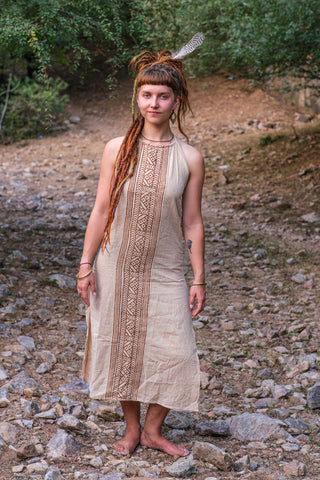 Full length front view of the beige Trishika block print khadi cotton halter maxi dress on a pebble riverbed