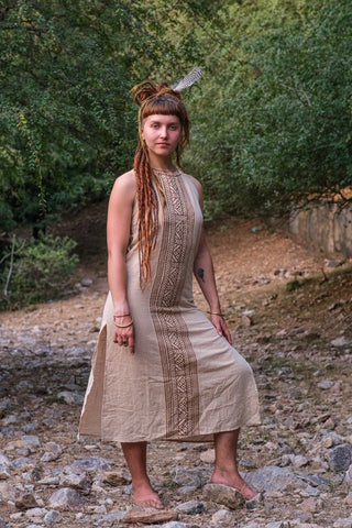 Woman modelling the Trishika beige halter maxi dress in block print, standing on stones by the water