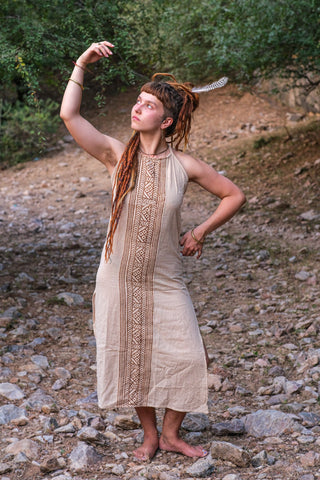 Model in the Trishika beige khadi maxi dress raising one arm by a wooded riverbank