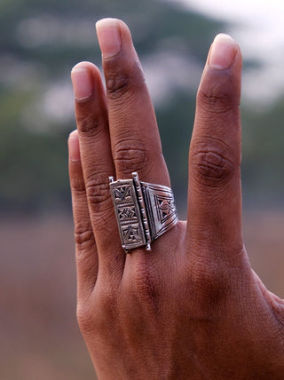 Back-of-hand view of the Tuareg ring worn outdoors with trees in the background, engraved panel catching the light