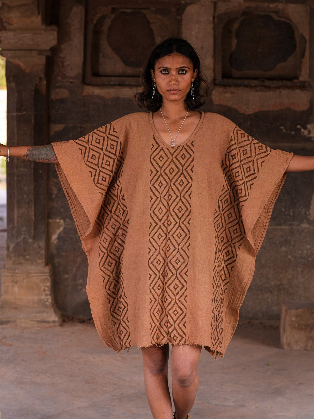 Tula kaftan in terracotta brown hand block print cotton, model with arms wide at heritage temple ruins, free-size boho dress