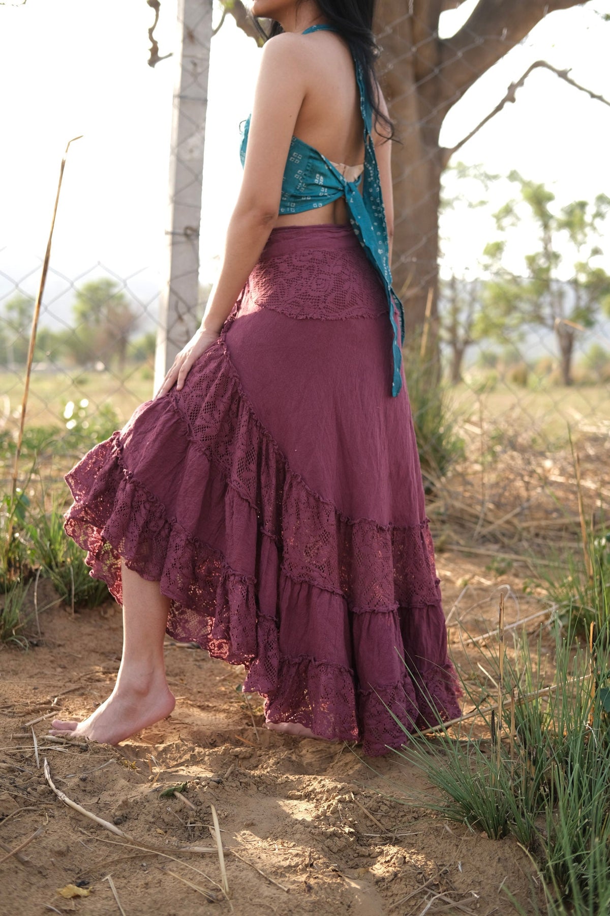 Back view of the wine red khadi cotton wrap skirt in a field, gathered tiers and scalloped lace edging falling straight