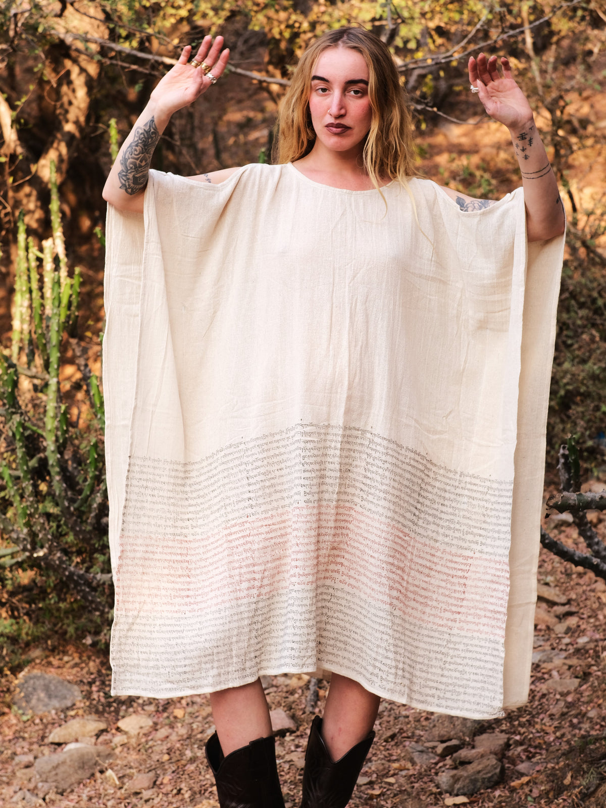 Free-size cream cotton Yaja Kaftan with script print, styled with black cowboy boots in the desert