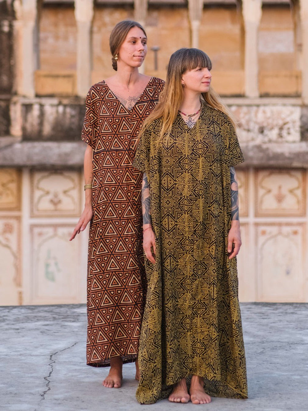 Two models wearing the Zuriya African print viscose kaftan in rust red and gold prints, front view, palace backdrop